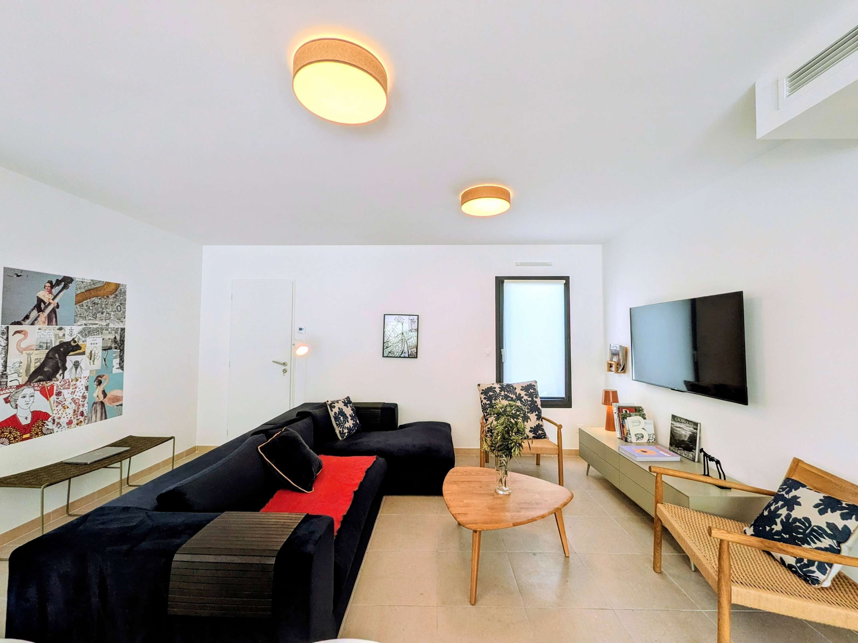 Ein modernes Wohnzimmer mit einem schwarzen Sofa, einem Holztisch, einem an der Wand montierten Fernseher und einem großen Fenster.