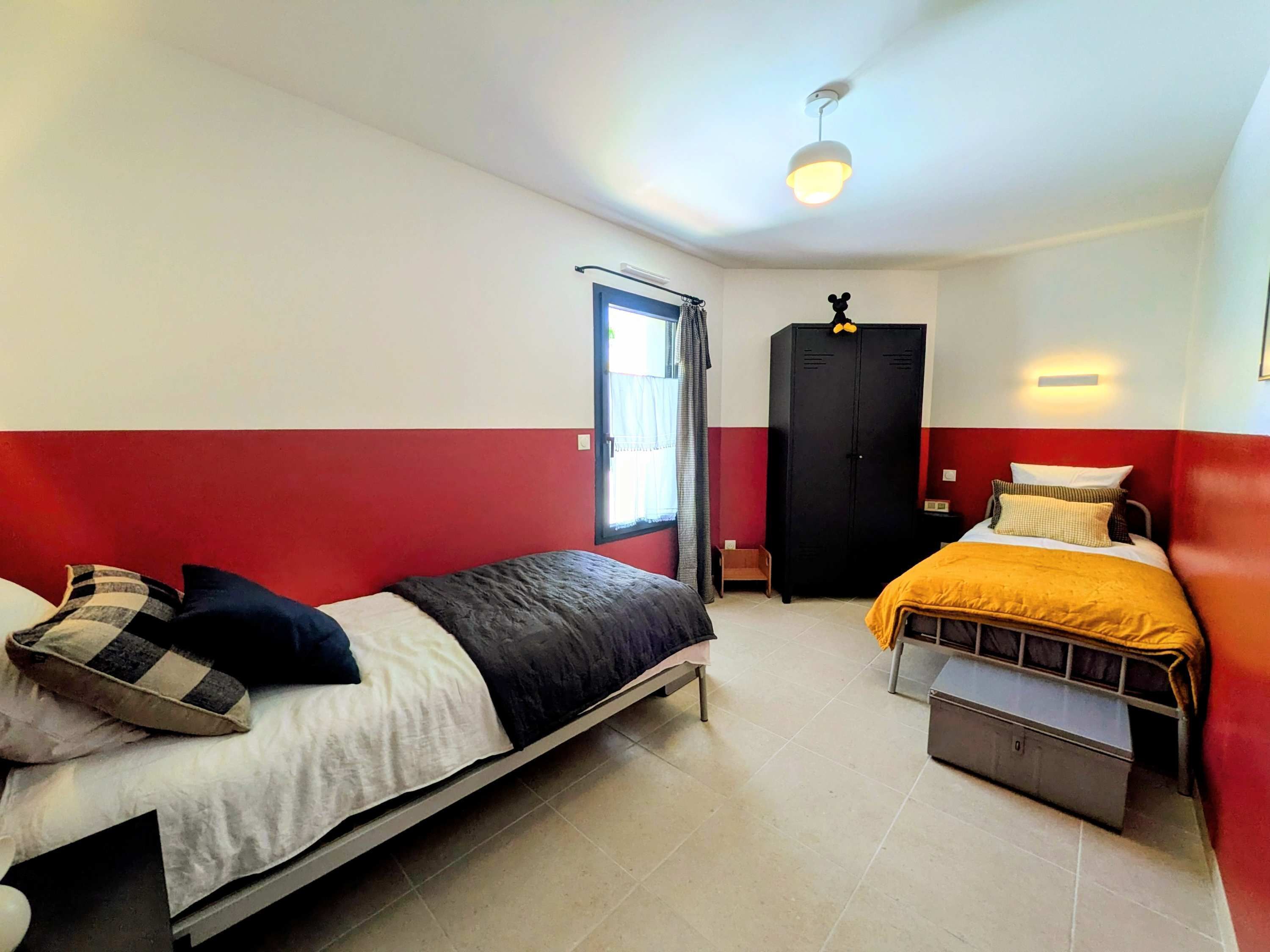 Un dormitorio con dos camas, un armario, una ventana con cortinas y una lámpara en el techo.