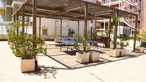 Ein Sitzbereich im Freien mit Tischen und Stühlen, umgeben von Topfpflanzen, unter einer Pergola.