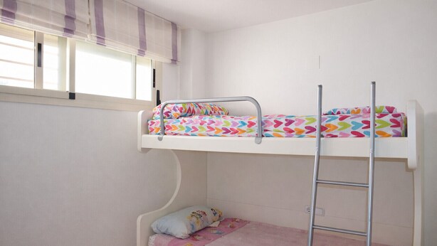 Ein Stockbett mit einer Leiter, ein Fenster mit Jalousien und ein Deckenventilator.