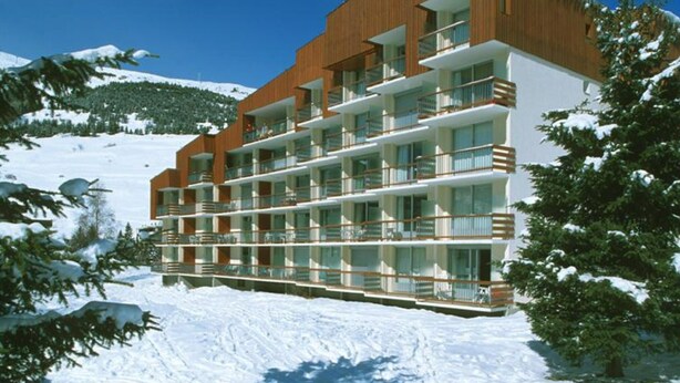 Un hotel de varios pisos con balcones, con vista a una montaña nevada.