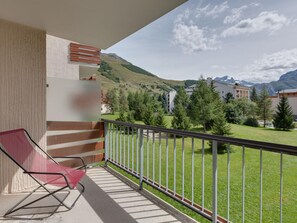 A balcony with a red chair, a view of a green landscape with trees and buildings, and a mountain in the background. - 1 BR Apartment for 6 in Les Deux Alpes (Les Deux Alpes)