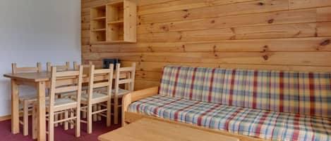 Un interior de madera con un sofá, sillas, una mesa y una estantería de pared.