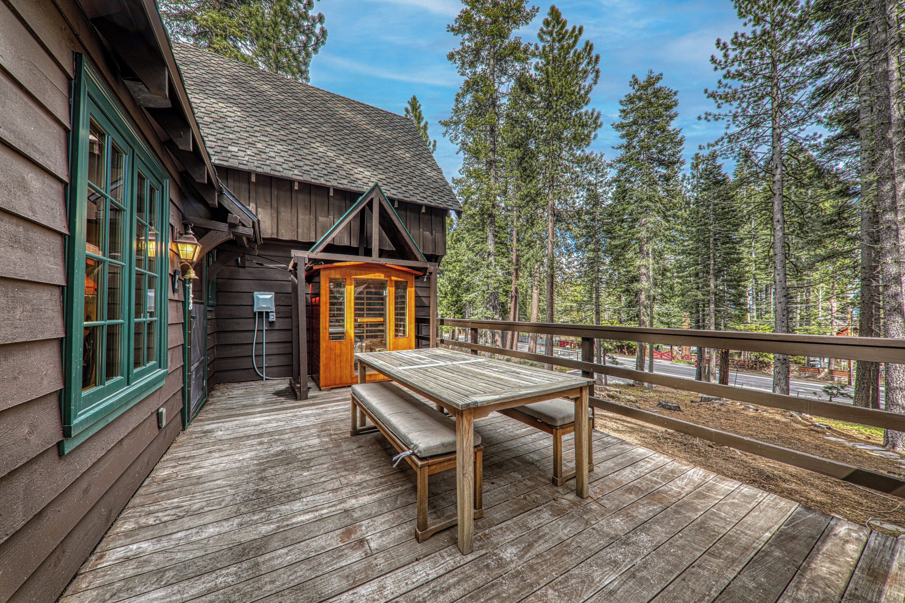 A wooden deck with a bench and table, surrounded by tall trees.