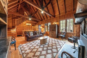 Ein rustikales Holzhaus-Interieur mit einer Holztreppe, einem Kamin, einer Couch und einem großen Fenster.