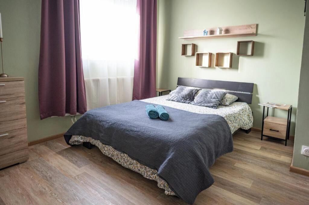 A bedroom with a bed, a dresser, a nightstand, and a window with curtains.