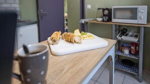Eine Küchenarbeitsplatte mit Schneidebrett, belegten Broten und Käse, einer Tasse und einer Mikrowelle auf einem Regal.