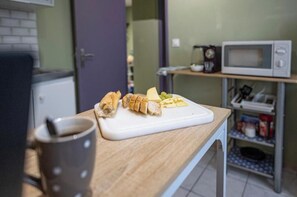 A kitchen counter with a cutting board holding sliced bread and cheese, a mug, and a microwave on a shelf. - Fanta Flat France Switzerland - Comfort & Quiet near Basel (Saint-Louis)
