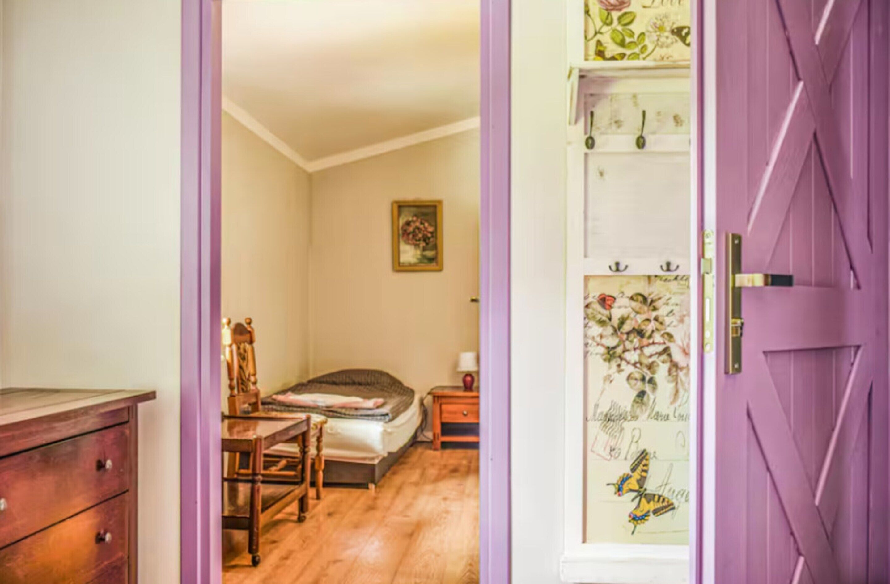 Una camera da letto con un letto, una sedia, una cassettiera e una porta con carta da parati floreale.