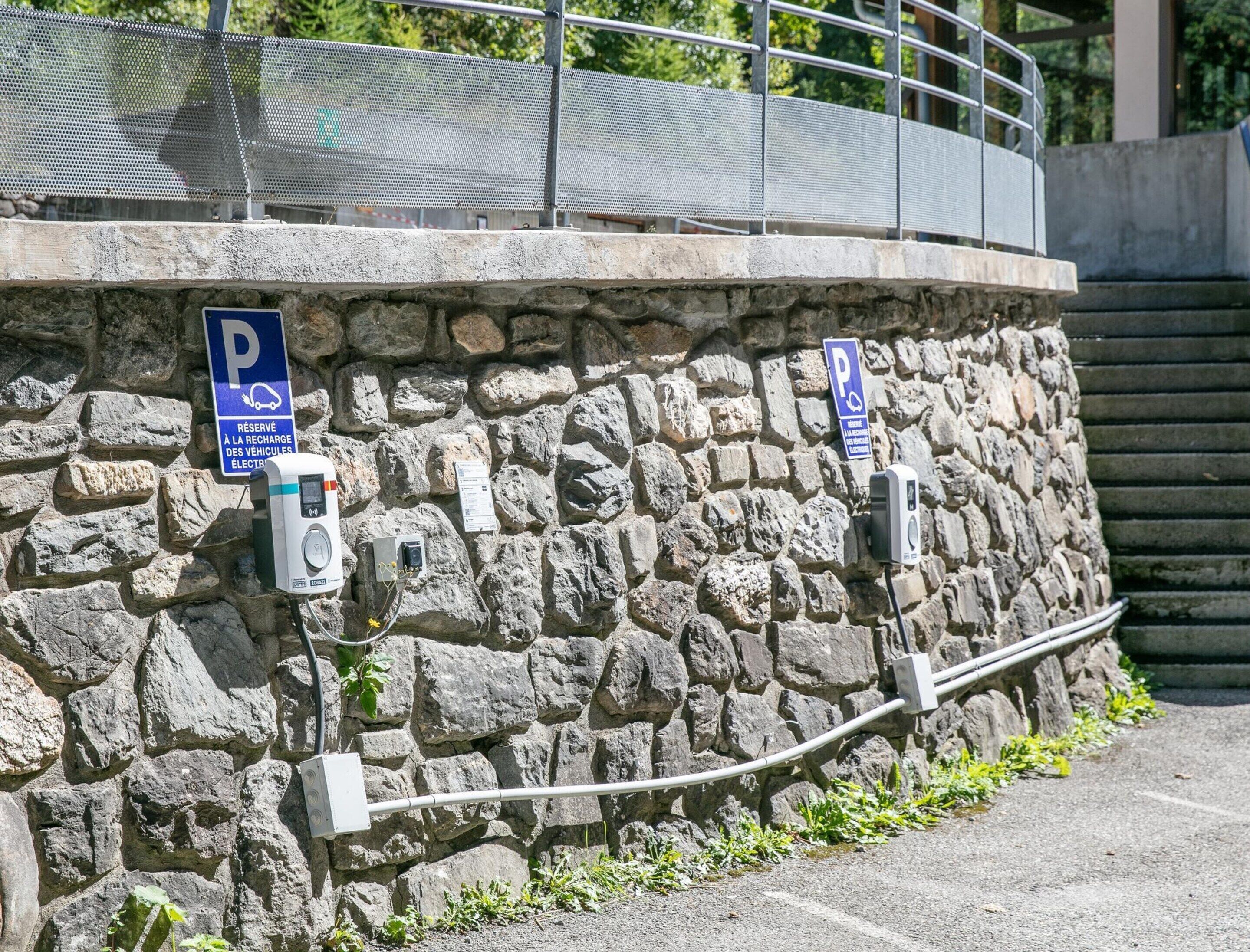 A stone wall with two parking signs, a metal fence, and a concrete curb.