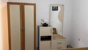 Een slaapkamer met een bed, een houten kledingkast, een nachtkastje met een spiegel en een klein kastje.