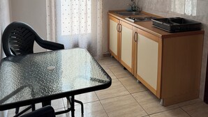 Een compacte keuken met een eettafel, stoelen, houten kastjes en een raam met gordijn.
