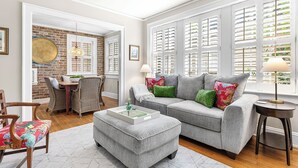 Ein Wohnzimmer mit grauem Sofa, Ottomanen und einem Essbereich mit Korbstühlen.