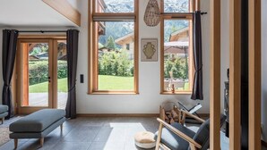 Una habitación amplia con ventanas grandes, un banco, una silla y una chimenea.