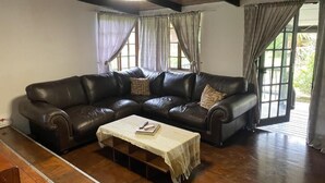 A living room with a large L-shaped leather sofa, a coffee table, and a ceiling light fixture. - Little Creek Cabins (Port Edward)