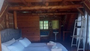 A wooden cabin room with a bed, a small table, and a chair. - Little Creek Cabins (Port Edward)