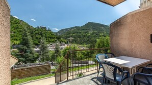 A balcony with a table and chairs, overlooking a village and mountains. - Spacious Apartment for 5-persons (Guillaumes)