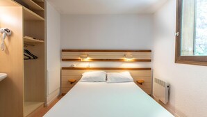 A small, narrow hotel room with a single bed, bedside tables, a wardrobe, and a window. - Spacious Apartment for 5-persons (Guillaumes)