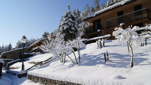 A snow-covered building with a stone retaining wall, a staircase, and snow-laden trees. - Spacious Apartment for 5-persons (Guillaumes)
