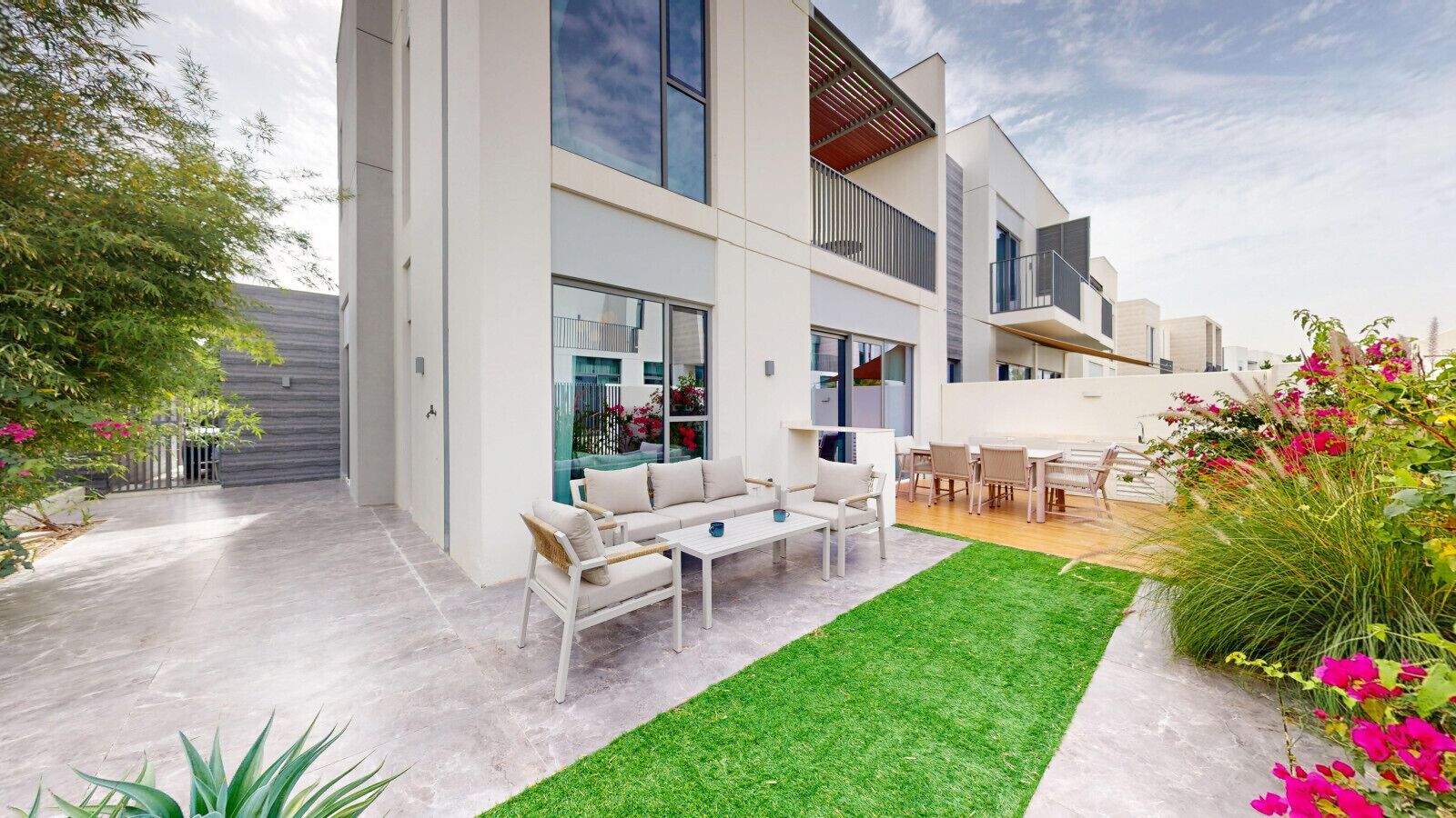 Una casa moderna con un patio, muebles de exterior y un jardín bien cuidado.