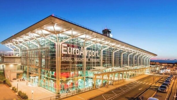 Terminal de aeroporto moderno com fachada de vidro, um sinalização EuroAirport em destaque e uma passarela coberta.
