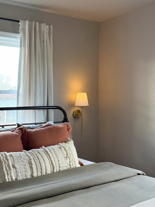 A neatly made bed with pillows, a bedside lamp, and a window with curtains. - The Sioux Stay, Beautiful New Home Near Downtown, Pet and Child Friendly (Sioux Falls)