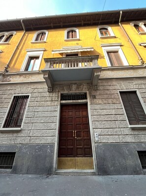 A building with a large wooden door, stone facade, and multiple windows with shutters. - Chloe's apartment 1 min walk from MM1 Pasteur/NoLo (Milano)