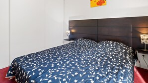 Une chambre à coucher avec un lit, une table de chevet, une lampe fixée au mur et un tableau.