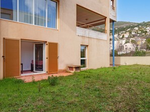Un edificio moderno de dos pisos con ventanas amplias, un balcón y vistas a un pueblo en la ladera.