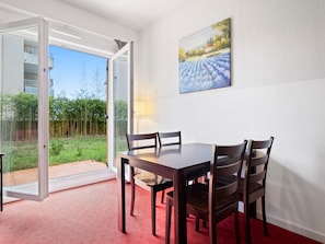 Un comedor con una mesa y sillas, un ventanal de vidrio que da a un jardín, y un cuadro en la pared.