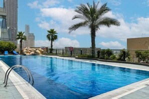 A swimming pool with a clear blue water, surrounded by palm trees and a cityscape in the background. - 1 Bed with Skyline Views l 41st Floor l Marina (Dubai Marina)