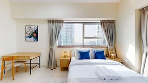 Hotelkamer met een bed, een bureau, een stoel, een nachtkastje met een lamp en een raam met gordijnen.