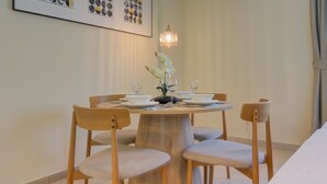 Een eethoek met een ronde tafel, vier stoelen, een vaas met bloemen en een aan de muur hangend schilderij.