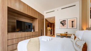 Quarto de hotel moderno com uma cama grande, televisão de tela plana, cozinha compacta e obras de arte na parede.