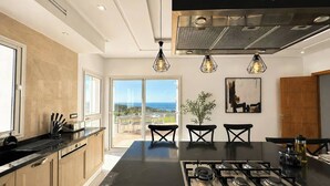 A modern kitchen with a central island, stainless steel appliances, and pendant lighting. - Azura House Sea View Pool (Metline)