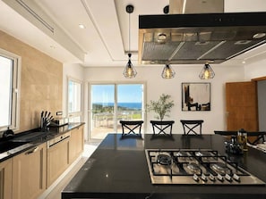 A modern kitchen with a central island, stainless steel appliances, and pendant lighting. - Azura House Sea View Pool (Metline)