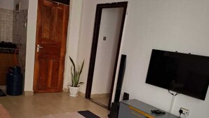 Ein Wohnzimmer mit Fernseher, Esstisch, Sofa und einer Topfpflanze.