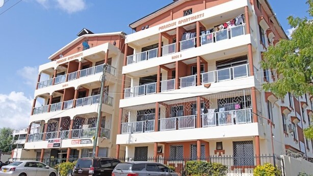 Ein mehrgeschossiges Gebäude mit Balkonen, einer Schilder mit der Aufschrift 'Paradise Apartments' und einem sichtbaren Geschäft namens 'Plus Point'.