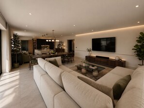 A modern living room with a large sofa, a coffee table, and a TV mounted on the wall. - Luxury 7 Bedroom Retreat Near Port Isaac - Sleeps 18 - Hot Tub & Games Room (Port Isaac)