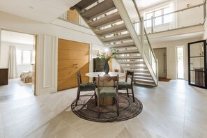 Ein geräumiges Zimmer mit Esstisch, Stühlen, einer großen Holztür und einer Treppe.