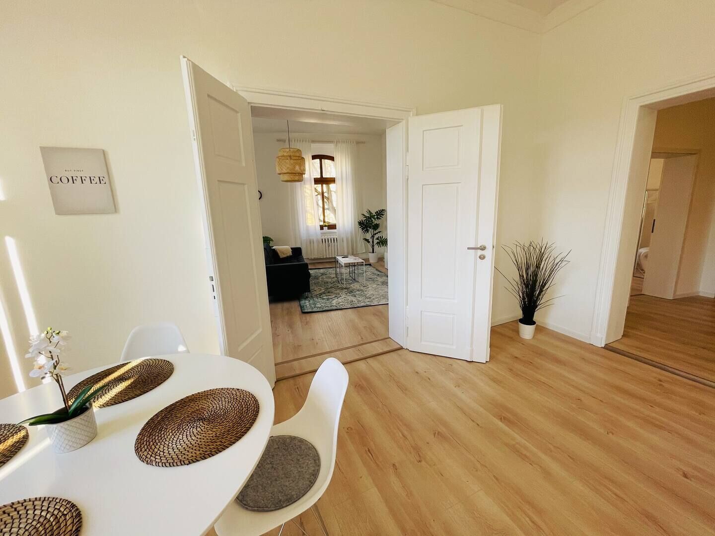 Una sala moderna con comedor, piso de madera y una puerta blanca que da a otra habitación.