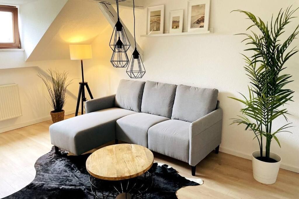 A modern living room with a grey sectional sofa, a round wooden coffee table, a black rug, a floor lamp, and a potted plant.