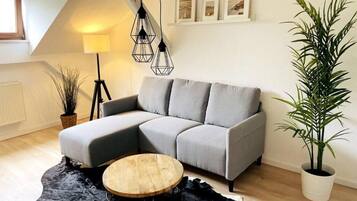 A modern living room with a grey sectional sofa, a round wooden coffee table, a black rug, a floor lamp, and a potted plant.