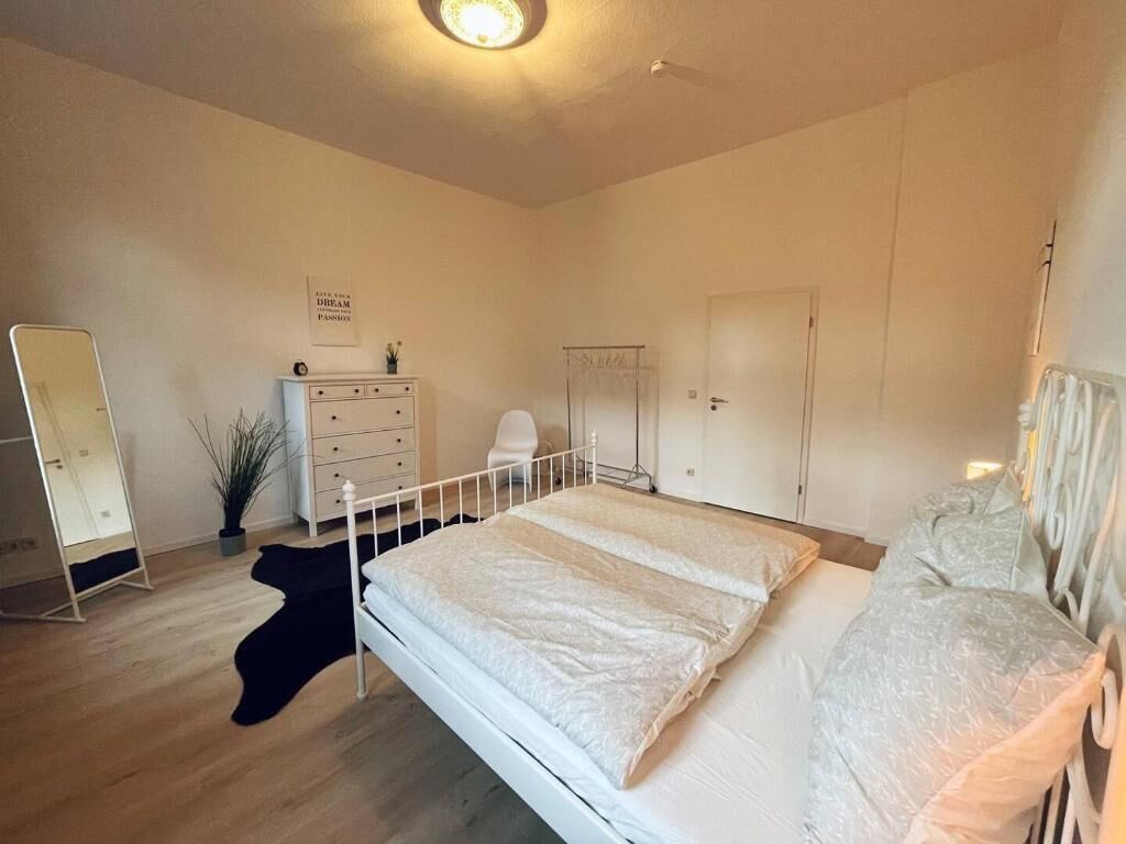 Une chambre à coucher avec un lit, une commode, un miroir et une porte.