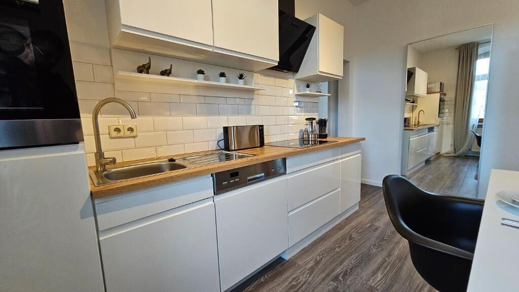 A modern kitchen with white cabinets, a stainless steel sink, and a wooden countertop.