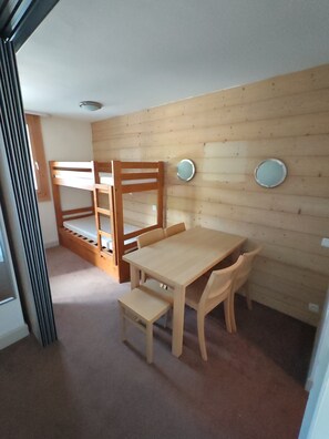 Ett rum med en våningssäng, ett träbord med stolar, en liten bänk och två runda speglar på väggen.