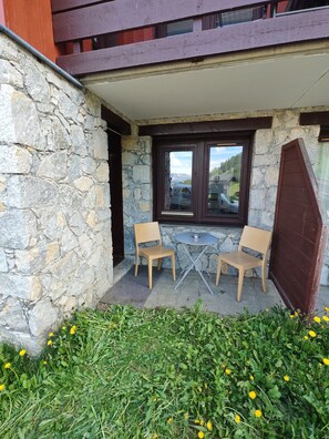 A stone wall, two wooden chairs, a small round table, and a view of a mountain through a window. - Le Nid des Silènes – In the Heart of the Cimes 1800 (La Plagne Tarentaise)