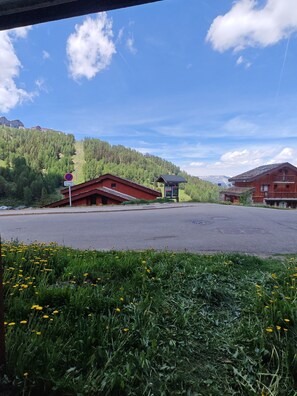 A rural road with a red building, a smaller structure, and a mountain backdrop. - Le Nid des Silènes – In the Heart of the Cimes 1800 (La Plagne Tarentaise)