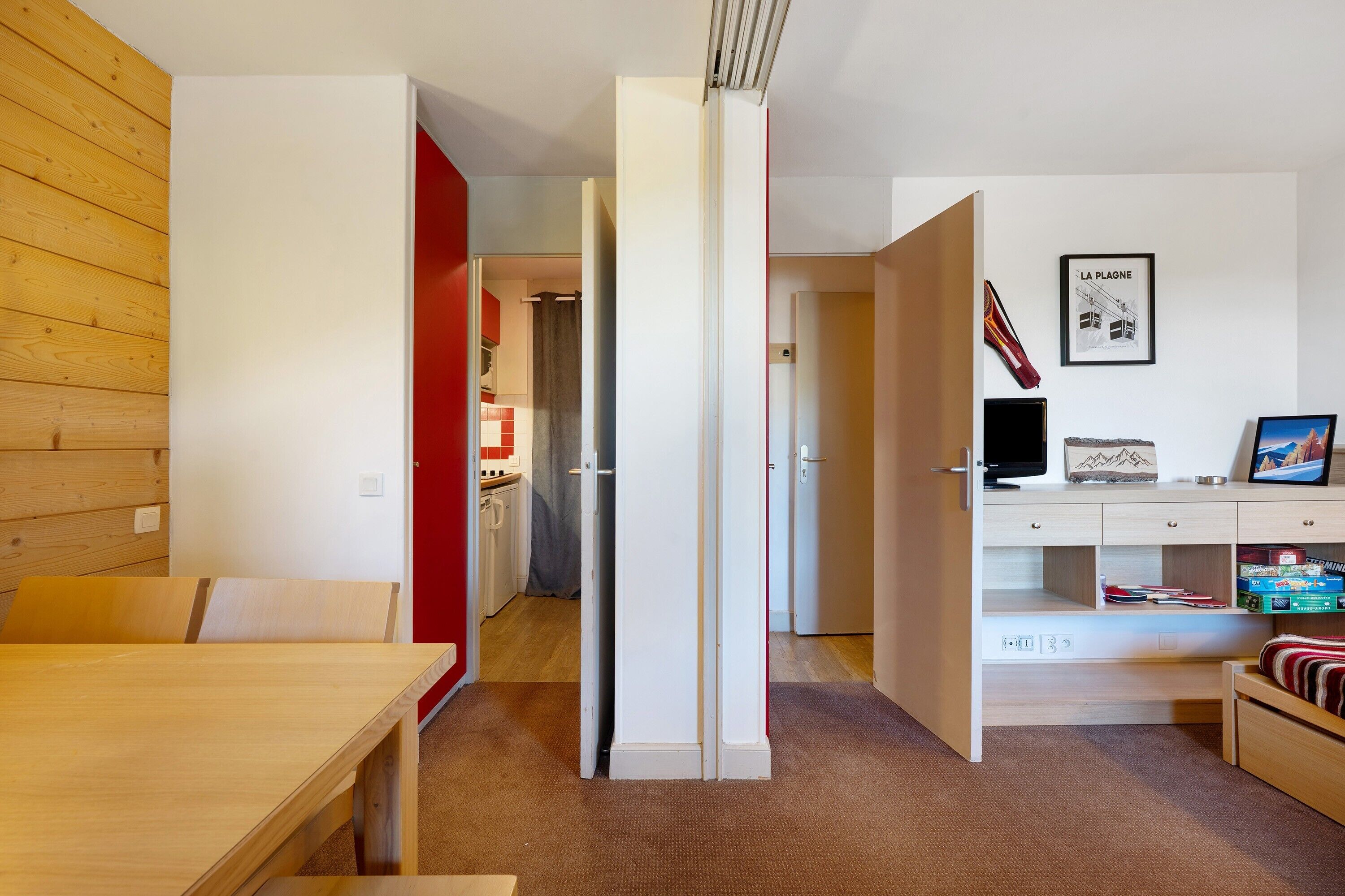 Una habitación moderna con una mesa de comedor de madera, un armario blanco, un escritorio con computadora y una cama con ropa de cama a rayas.