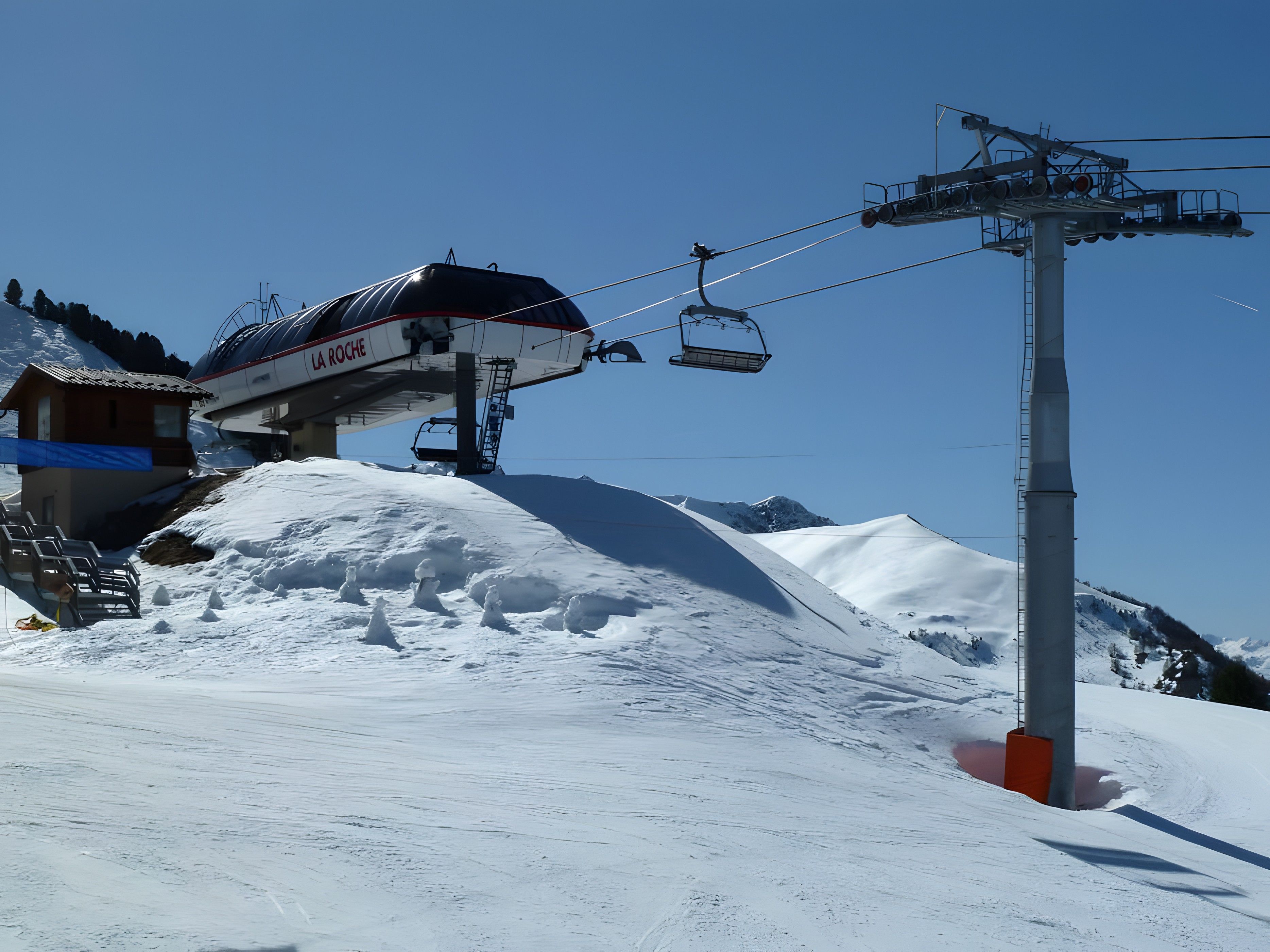 Een skilift met een stoeltjeslift en een gebouw met de tekst 'A ROCHE' op de achtergrond.